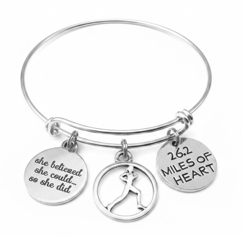 Silver expandable bangle bracelet with She Believed She Could disc charm, female runner silhouette circle charm, and 26.2 Miles of Heart disc charm on white background — marathon gift for her by Jules Obsession"