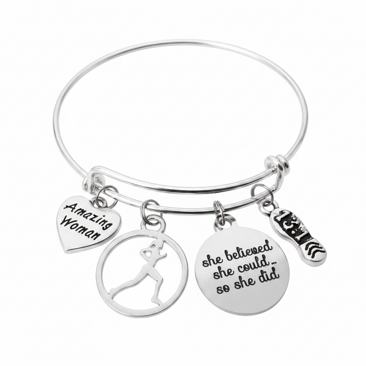 Silver-plated expandable wire bangle bracelet with four charms: heart charm engraved Amazing Woman, circular cutout female runner silhouette charm, round disc charm engraved she believed she could so she did, and 13.1 running shoe charm — motivational marathon gift for women runners