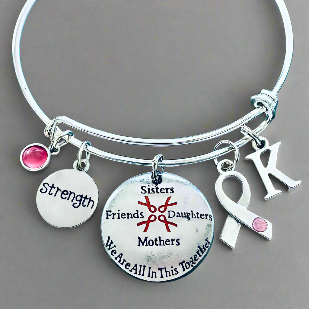 Silver bracelet with charms including a pink ribbon, 'Strength', 'Sisters Friends Daughters Mothers We Are All In This Together' 
