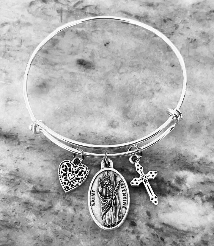 Expandable silver Saint Valentine charm bracelet with heart and cross on silver-tone bangle