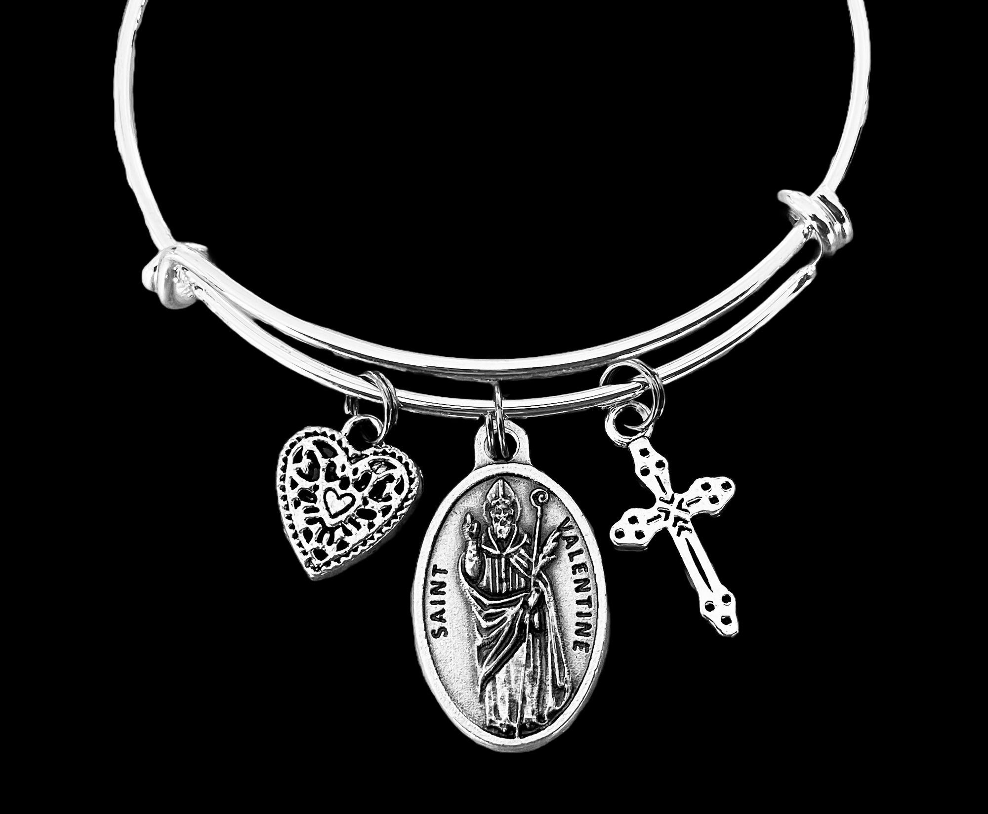 Silver bracelet with charms including a heart, Saint Valentine, and cross on a black background