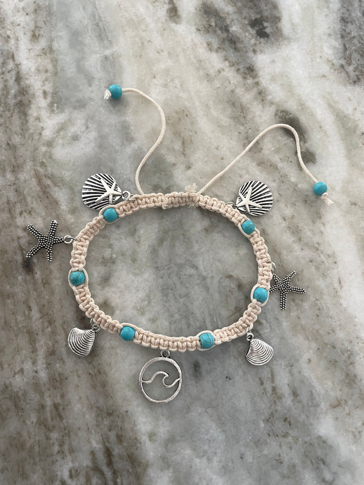 Macrame bracelet with shell, starfish, and wave charm on a marble background