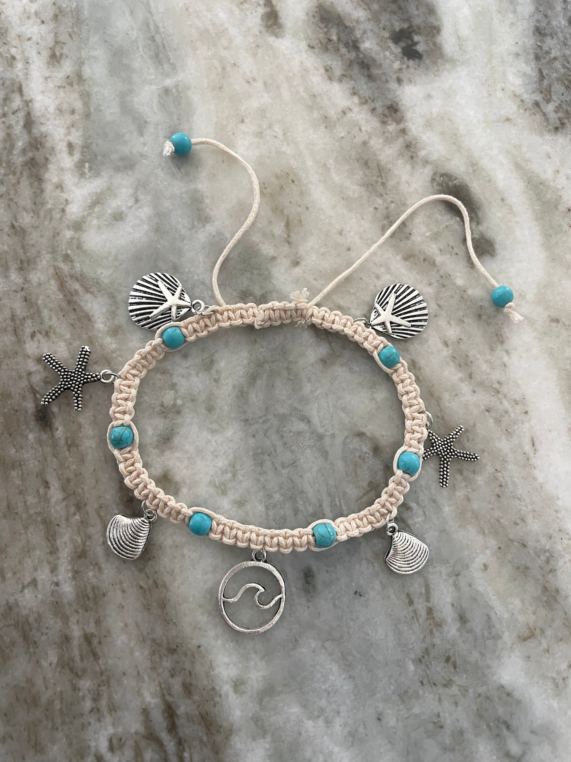 Macrame bracelet with shell, starfish, and wave charm on a marble background