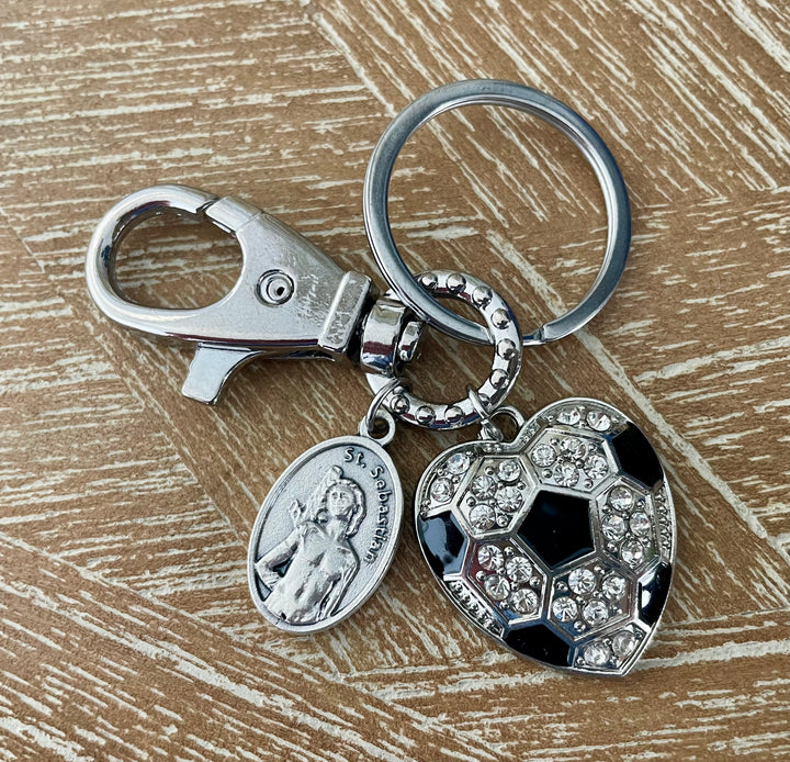 Close-up of Saint Sebastian medal and crystal soccer heart charm keychain on wooden surface – Christian athlete gift"