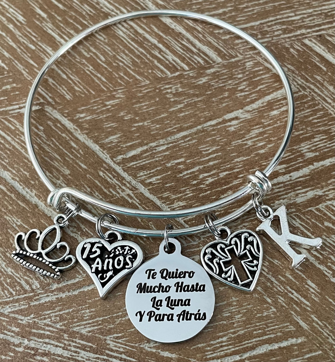 Personalized Silver expandable bangle bracelet with crown charm, 15 Años heart charm, Te Quiero Mucho Hasta La Luna engraved disc, filigree cross charm, and personalized initial charm — meaningful Quinceañera gift for girls