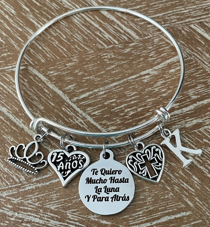 Personalized Silver expandable bangle bracelet with crown charm, 15 Años heart charm, Te Quiero Mucho Hasta La Luna engraved disc, filigree cross charm, and personalized initial charm — meaningful Quinceañera gift for girls