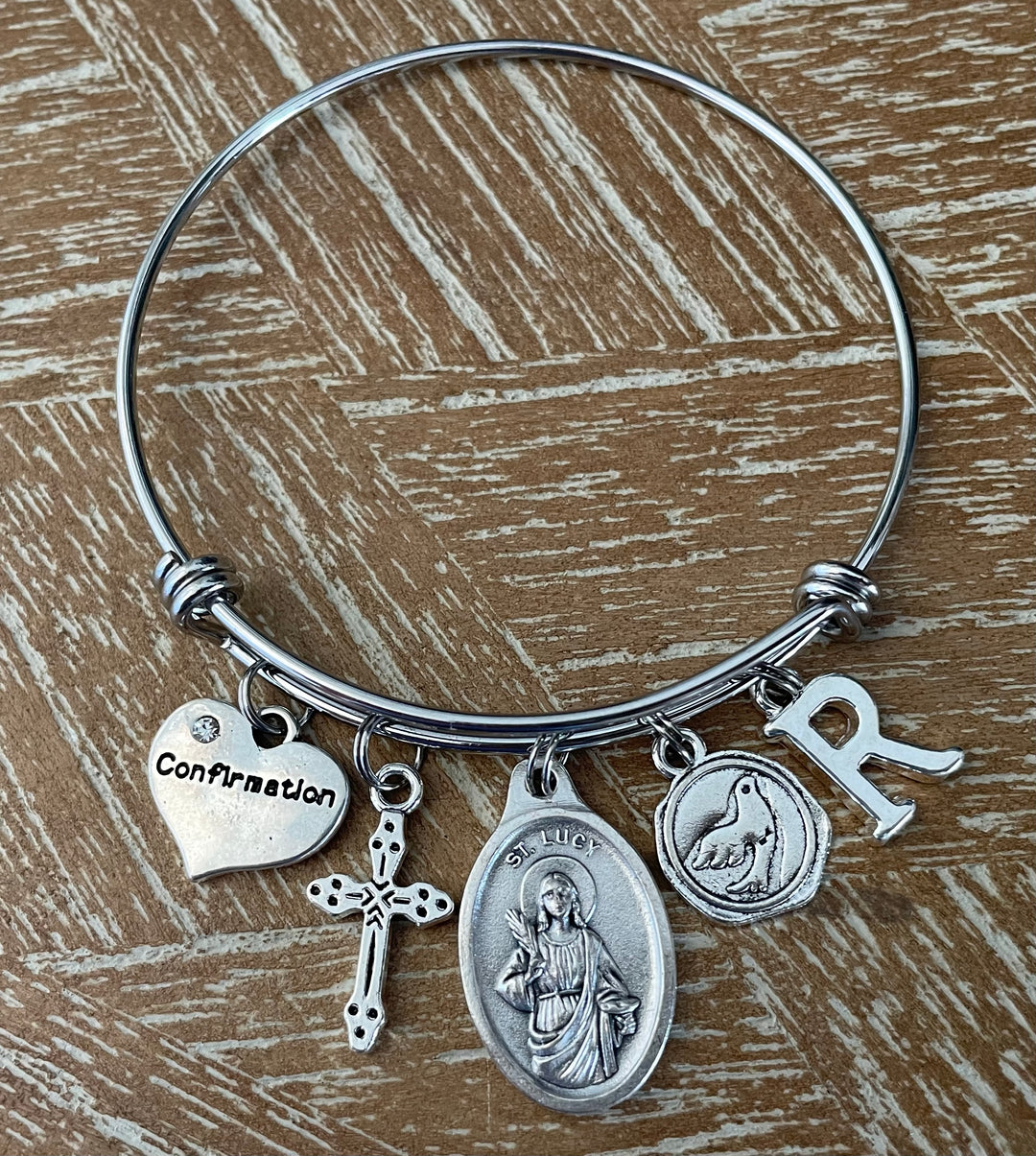 Confirmation charm bangle bracelet with St. Lucy oval saint medal, cross charm, dove medallion, Confirmation heart, and letter initial charm 