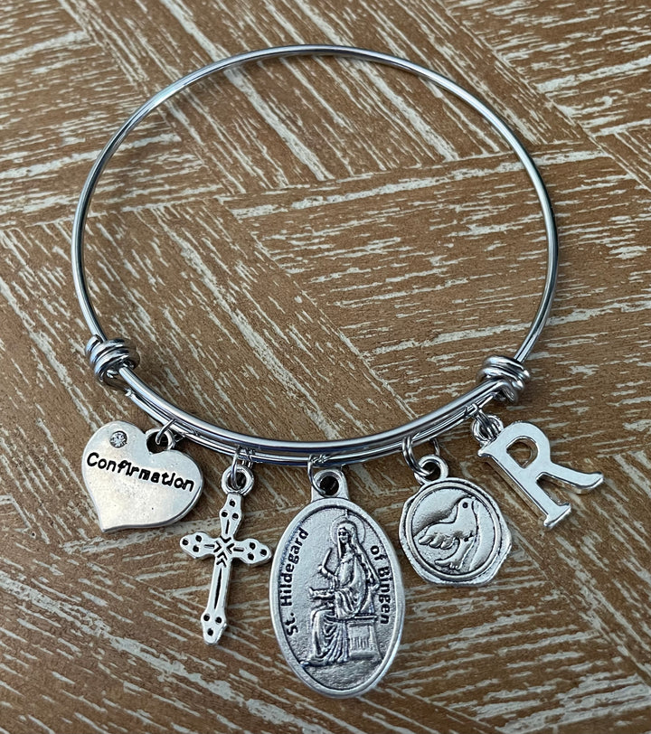 Confirmation charm bangle bracelet with St. Hildegard of Bingen saint medal, decorative cross, dove charm, Confirmation heart, and letter R initial charm