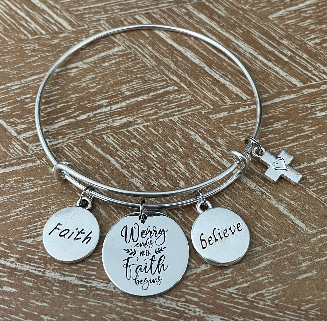 Professional studio photo of silver faith charm bangle bracelet with engraved Faith, Believe, Worry Ends When Faith Begins discs and cross charm on white background — Jules Obsession