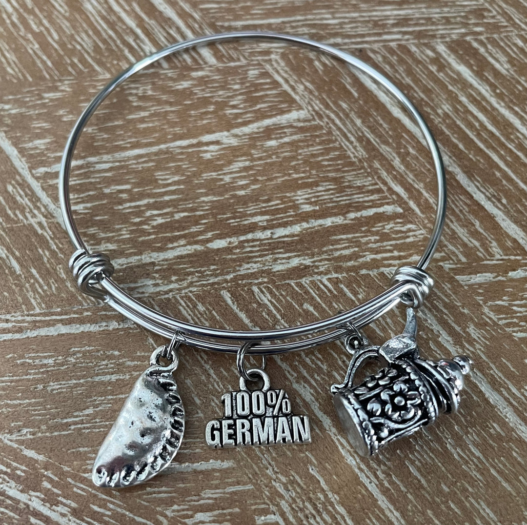 A silver-tone bangle bracelet with three charms: a semolina pastry, a small beer mug, and a charm reading &