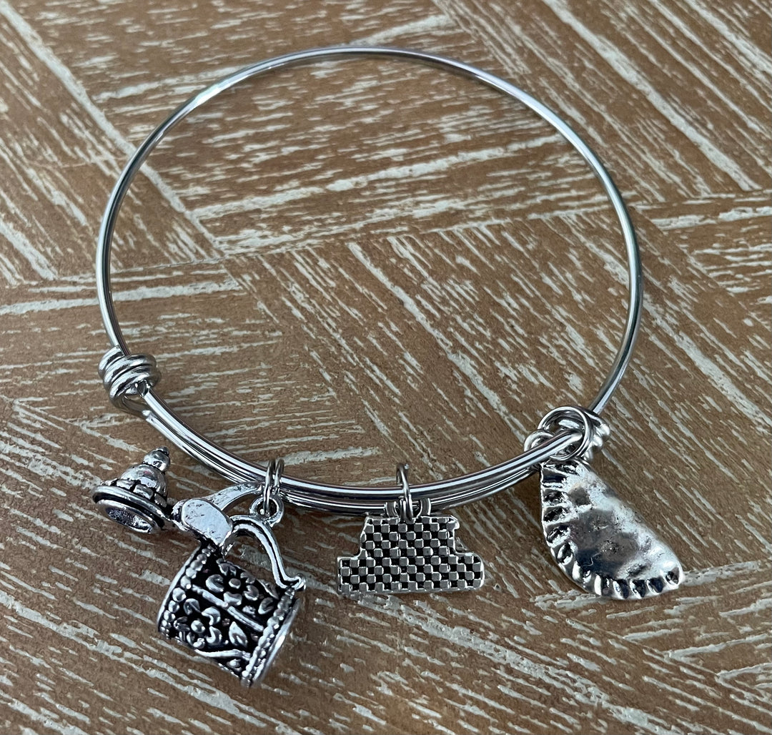 A silver wire charm bracelet. The bracelet features three distinct charms: a miniature Beer Stein, Perogi and 100% German Charm