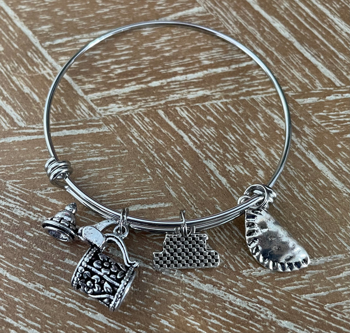 A silver wire charm bracelet. The bracelet features three distinct charms: a miniature Beer Stein, Perogi and 100% German Charm