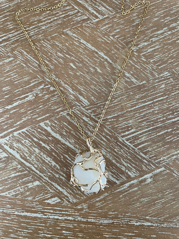 A delicate gold chain necklace with a unique pendant featuring a white, textured stone wrapped in organic, branch-like gold wire, displayed on a rustic wood background.