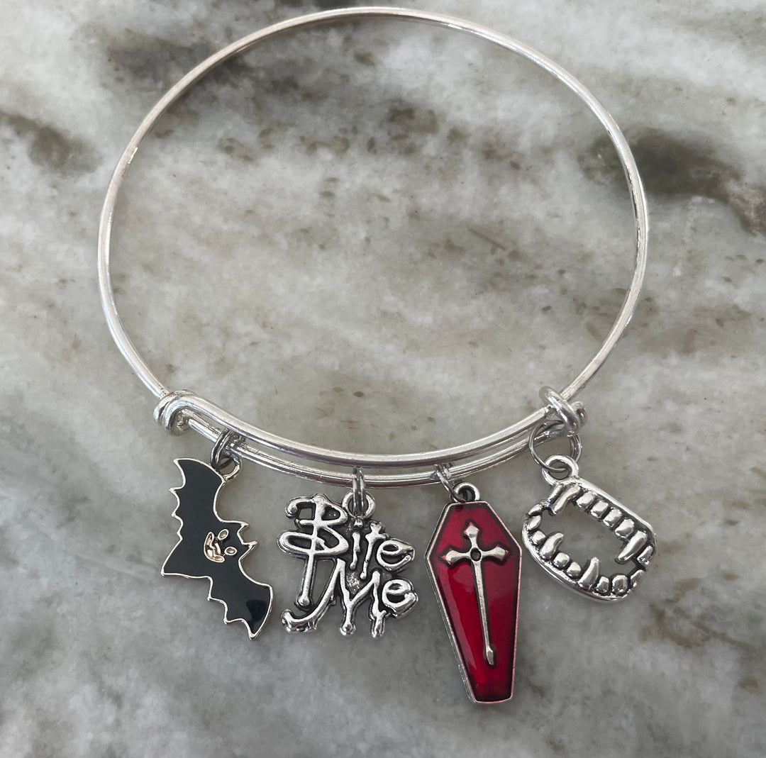 A silver charm bangle bracelet featuring four gothic-themed charms: a black bat words &