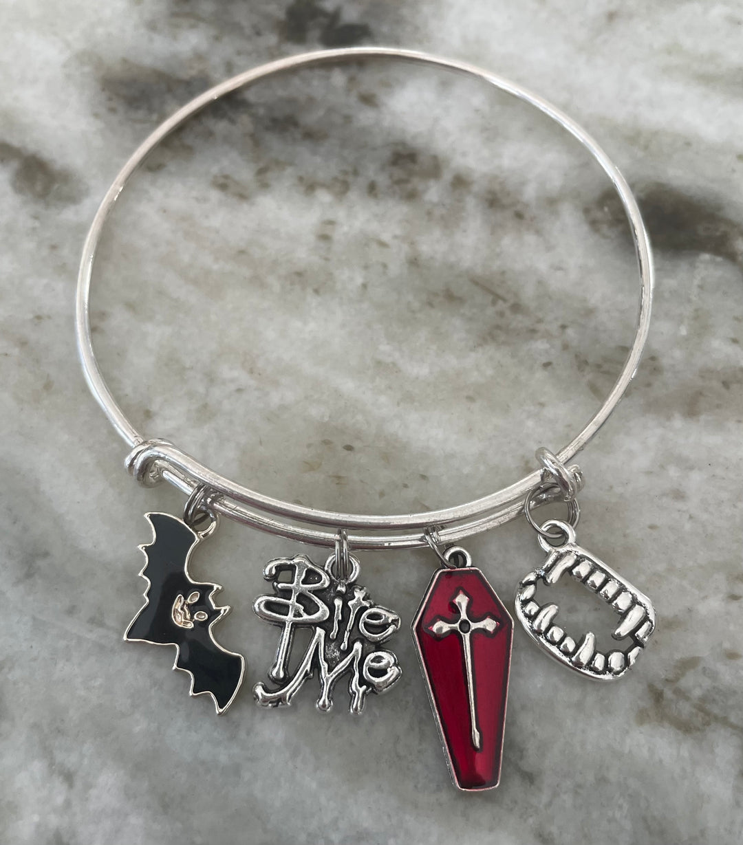 A silver-tone bangle bracelet with four Halloween-themed charms: a black bat, &