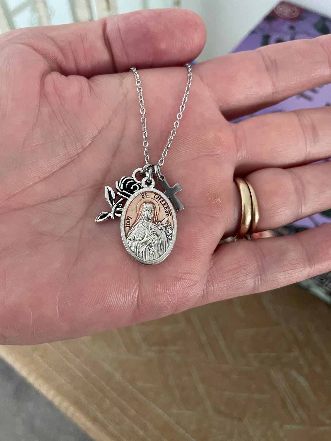 St. Therese of Lisieux Italian oval medal charm with rose-gold enamel center, raised silver border, and accompanying silver rose bud and cross charms on stainless steel chain