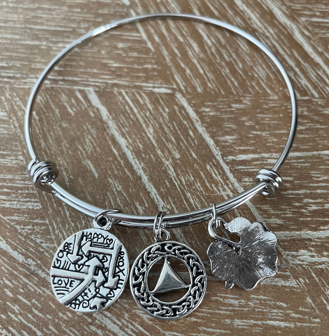 A silver bangle bracelet with three dangling charms, AA Symbol, Dragonfly, Quote