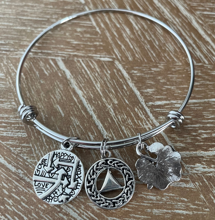 A silver bangle bracelet with three dangling charms, AA Symbol, Dragonfly, Quote
