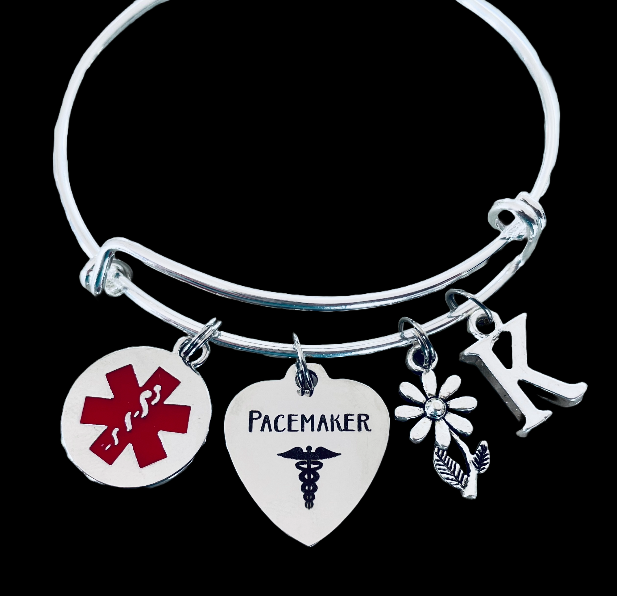 Silver expandable pacemaker medical alert bracelet with red symbol, heart charm engraved “Pacemaker,” daisy flower, and initial charm.