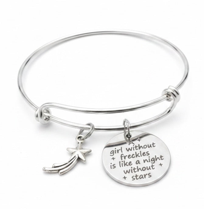 Silver expandable bangle bracelet with shooting star charm and engraved disc reading a girl without freckles is like a night without stars on white background by Jules Obsession
