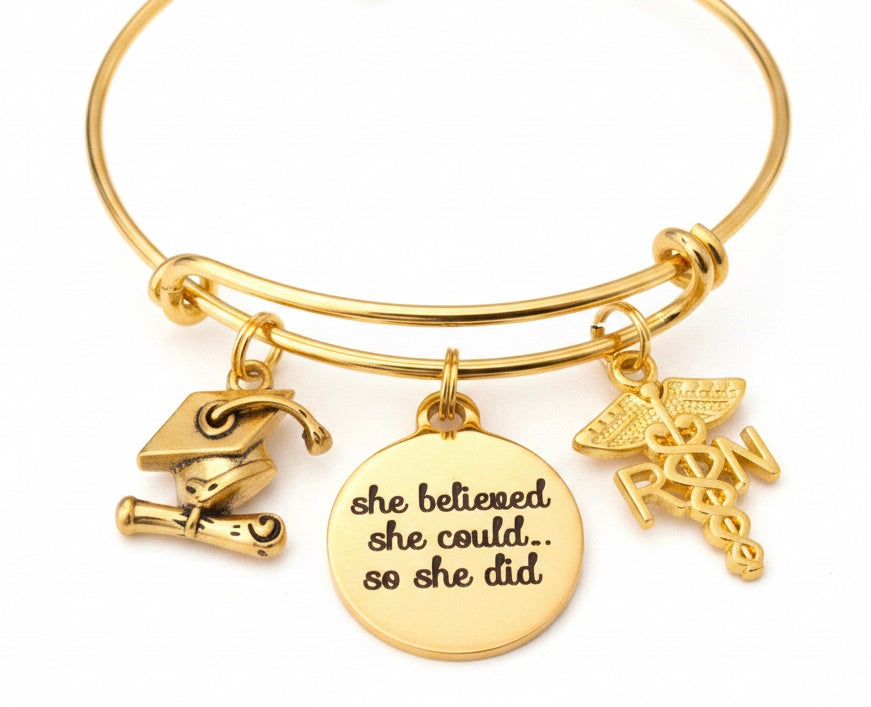 Gold RN nurse graduation charm bracelet with graduation cap diploma charm, RN caduceus charm, and She Believed She Could So She Did engraved disc charm on adjustable gold bangle – Jules Obsession