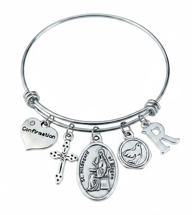 Confirmation charm bangle bracelet featuring St. Hildegard of Bingen medal, cross charm, dove charm, Confirmation heart, and personalized initial charm in silver