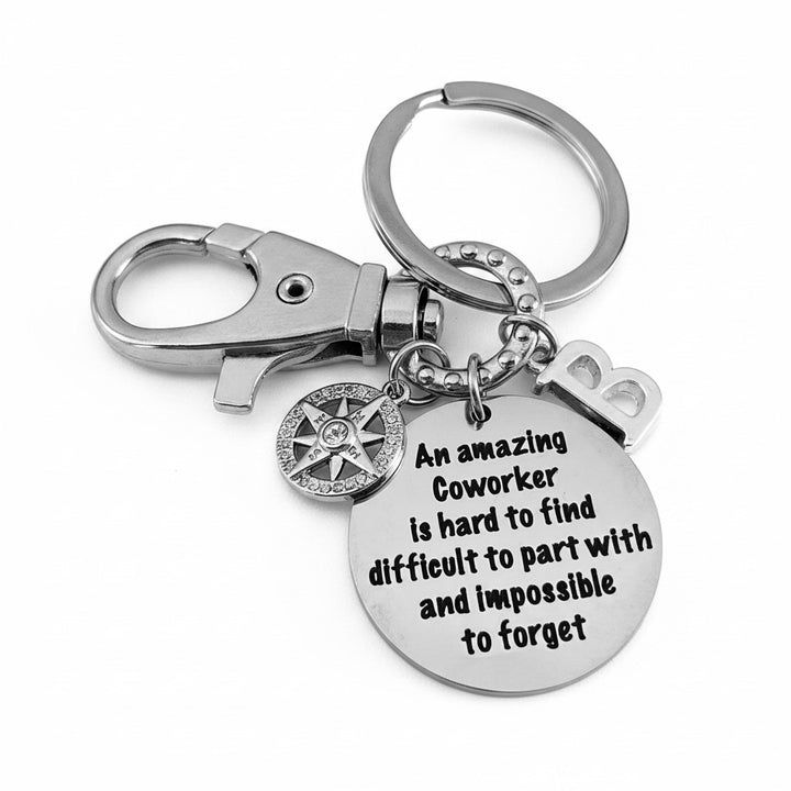Silver personalized coworker keychain with engraved quote disc reading "An amazing Coworker is hard to find, difficult to part with, and impossible to forget," crystal compass rose charm, and letter initial charm — displayed on a white background.