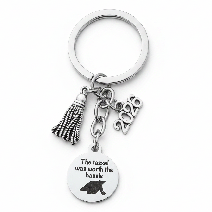 Silver graduation keychain held in hand showing tassel charm, 2026 year charm, and engraved disc reading The tassel was worth the hassle with graduation cap, Class of 2026 gift