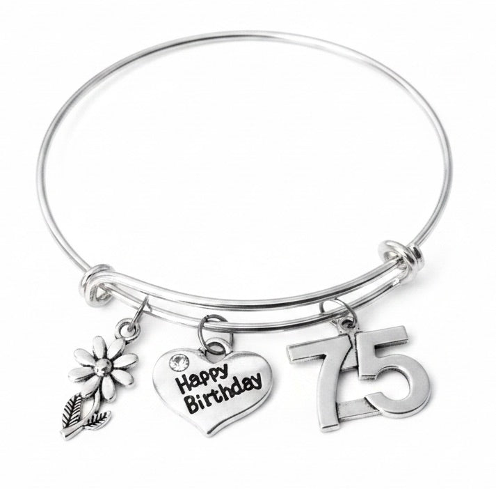 Silver-plated expandable wire bangle bracelet with three charms: silver daisy flower charm, heart charm engraved Happy Birthday with crystal rhinestone center, and bold silver 75 number charm — meaningful milestone birthday gift for women turning 75