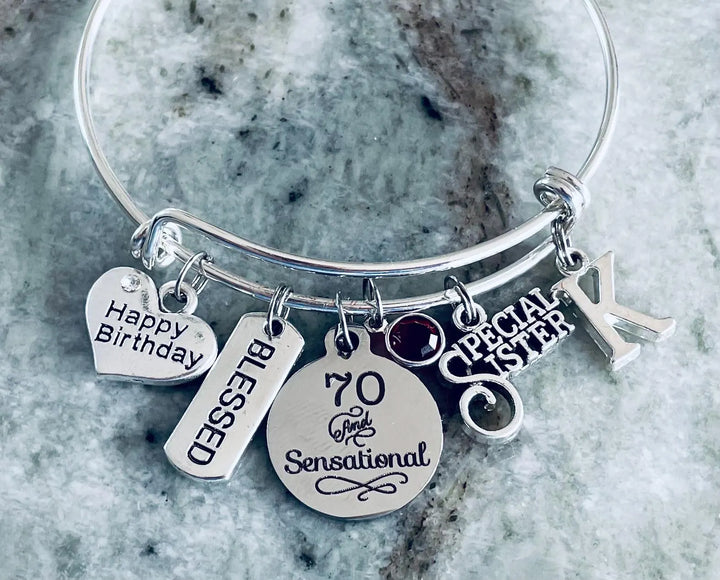 A silver charm bangle. The bracelet features multiple engraved charms, including a heart-shaped &