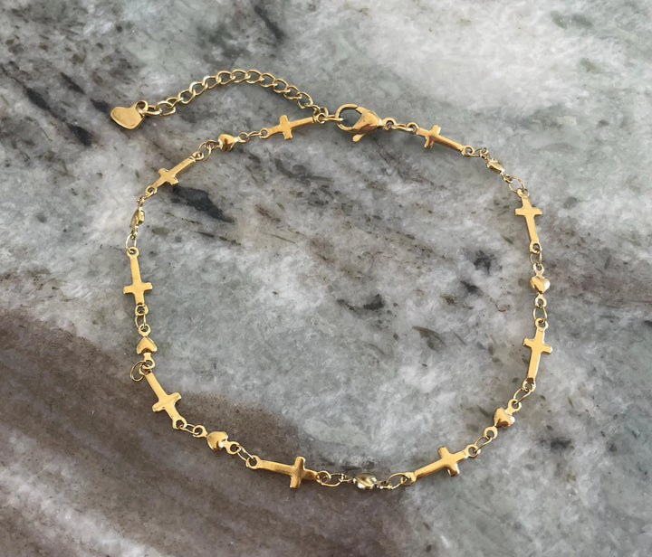 Delicate gold-tone stainless steel anklet featuring alternating flat cross charms and small heart links on a fine chain, with a lobster clasp and heart extender charm — displayed on a white background.