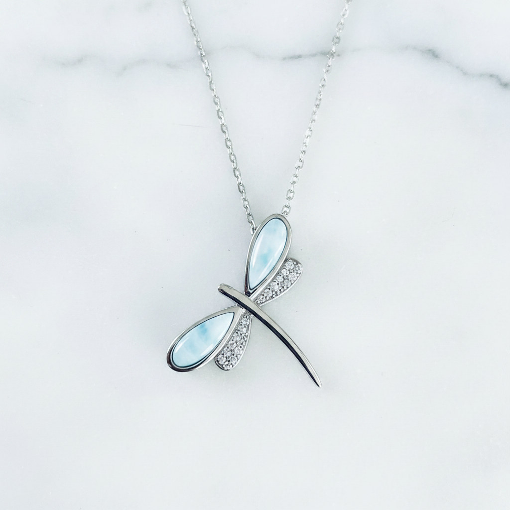 Sterling silver dragonfly pendant necklace with genuine Dominican larimar blue wings and pavé crystal rhinestone wings on a white surface