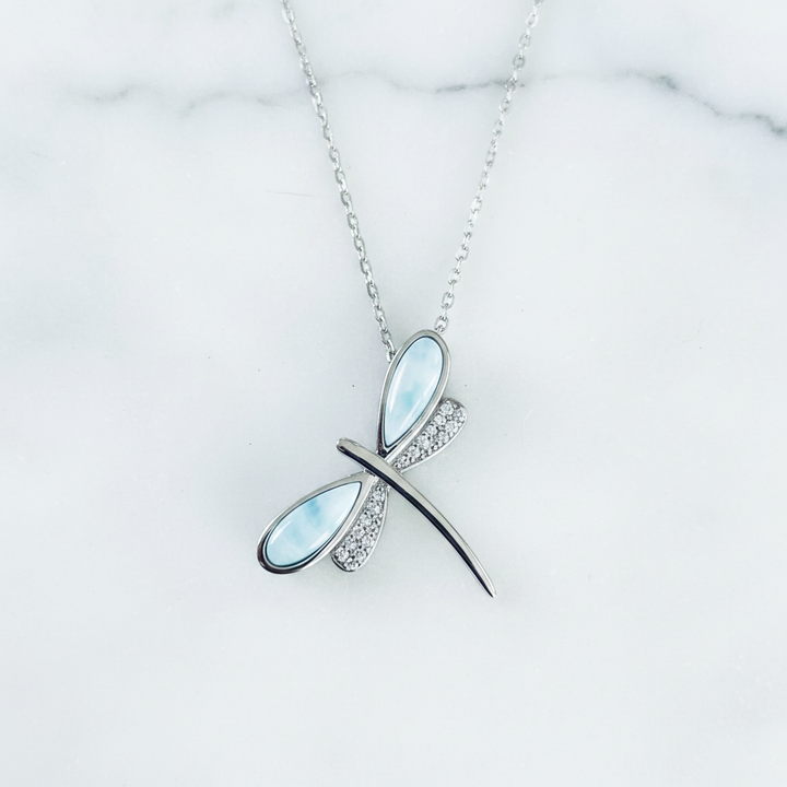 Sterling silver dragonfly pendant necklace with genuine Dominican larimar blue wings and pavé crystal rhinestone wings on a white surface