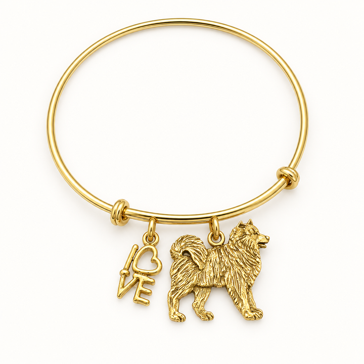 Gold bangle bracelet with a fluffy dog charm and a LOVE script charm, shown on a warm-white studio background