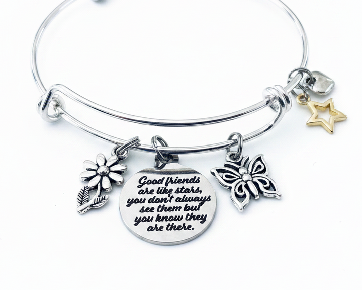 Silver expandable charm bangle bracelet with daisy flower charm, butterfly charm, gold star charm, and round engraved quote disc reading Good Friends Are Like Stars handcrafted by Jules Obsession