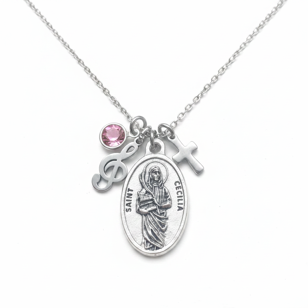 Silver Saint Cecilia oval medal necklace with treble clef music charm, cross charm, and pink faceted crystal birthstone on stainless steel cable chain, white studio background