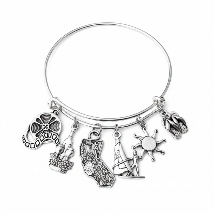 Silver expandable bangle bracelet with six California-themed charms: film reel, wine bottle with grapes, California state shape with city names, windsurfer, sun, and flip flops — adjustable stackable gift bracelet for California lovers and women