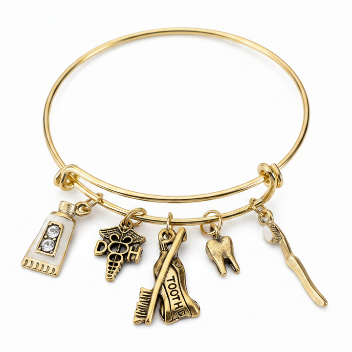 Gold-tone expandable bangle bracelet with five dentistry charms — toothpaste tube, dental caduceus, tooth extraction, molar tooth, and dental pick — on white studio background