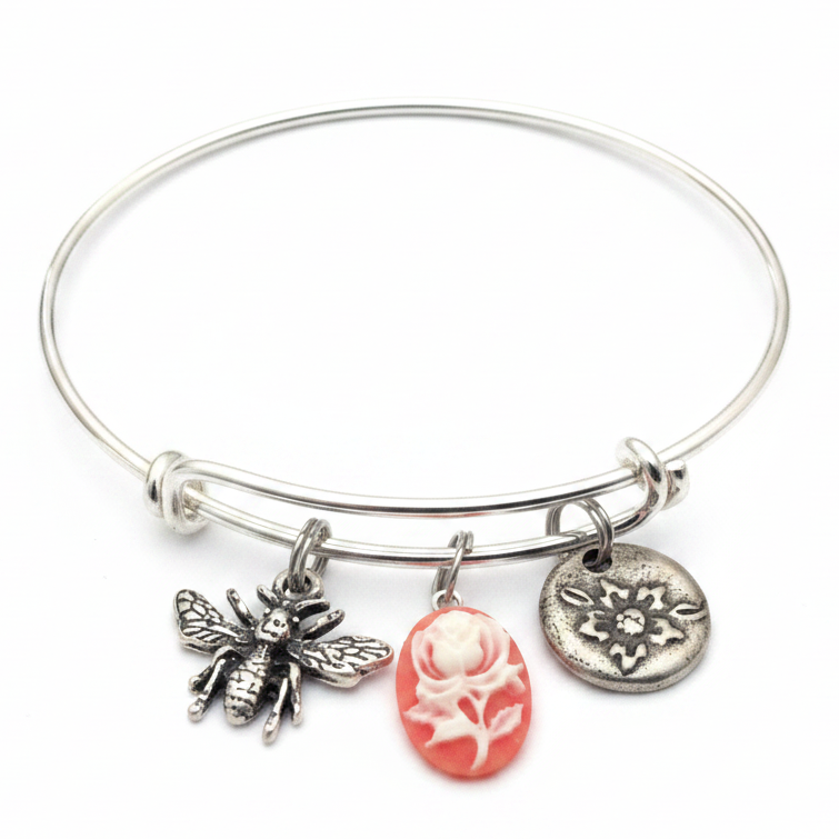 Silver expandable bangle bracelet with three charms: detailed silver honeybee with textured wings, round embossed silver flower disc, and pink oval cameo with white rose relief carving — adjustable stackable vintage style gift bracelet for women