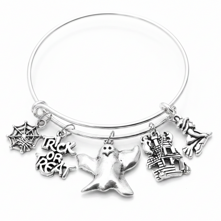 Silver adjustable bangle bracelet with five Halloween charms including spider web, Trick or Treat text, ghost, haunted house, and witch on a white studio background