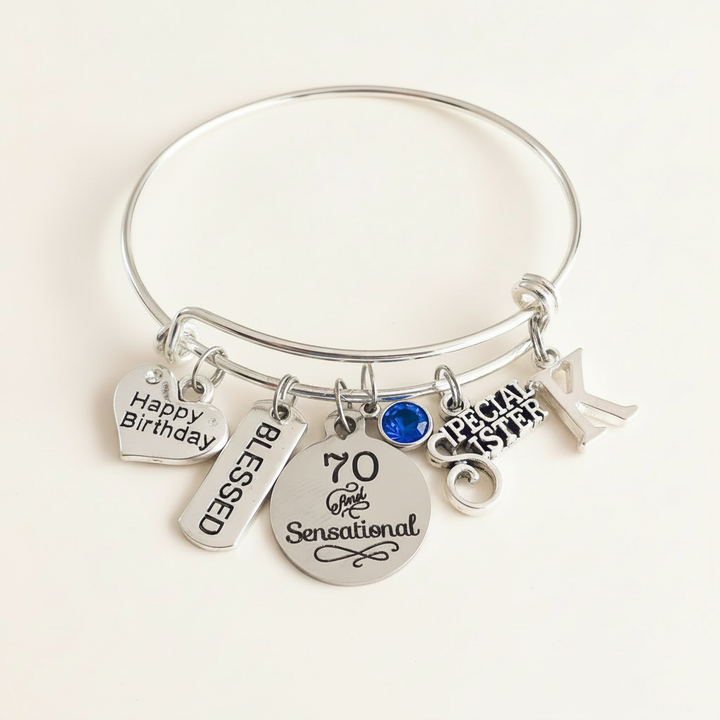 Silver bangle bracelet with engraved Happy Birthday, Blessed, 70 and Special Sister charms, featuring a royal-blue birthstone on a clean white studio background