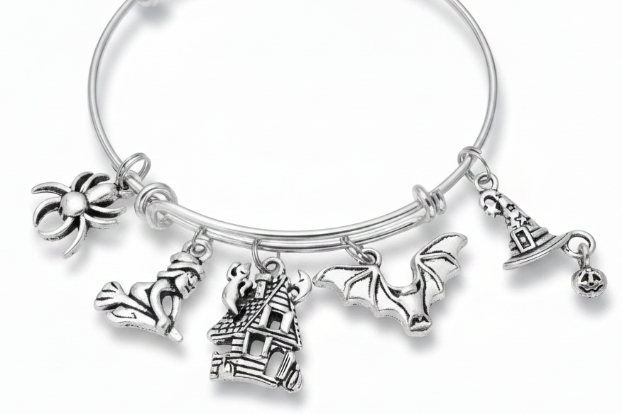 Silver expandable wire bangle bracelet on white background featuring seven Halloween charms: spider, witch on broomstick, ghost, haunted house, bat with spread wings, witch hat, and jack-o-lantern pumpkin