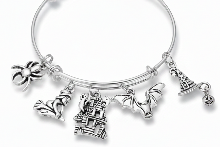 Silver expandable wire bangle bracelet on white background featuring seven Halloween charms: spider, witch on broomstick, ghost, haunted house, bat with spread wings, witch hat, and jack-o-lantern pumpkin