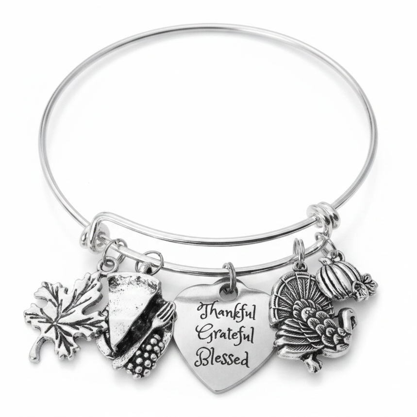 Silver expandable wire bangle bracelet on white background featuring four Thanksgiving charms: maple leaf, cornucopia, Thankful Grateful Blessed engraved heart, and Thanksgiving turkey with full tail feathers and pumpkin