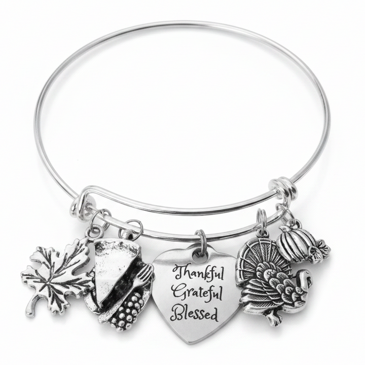 Silver expandable wire bangle bracelet on white background featuring four Thanksgiving charms: maple leaf, cornucopia, Thankful Grateful Blessed engraved heart, and Thanksgiving turkey with full tail feathers and pumpkin