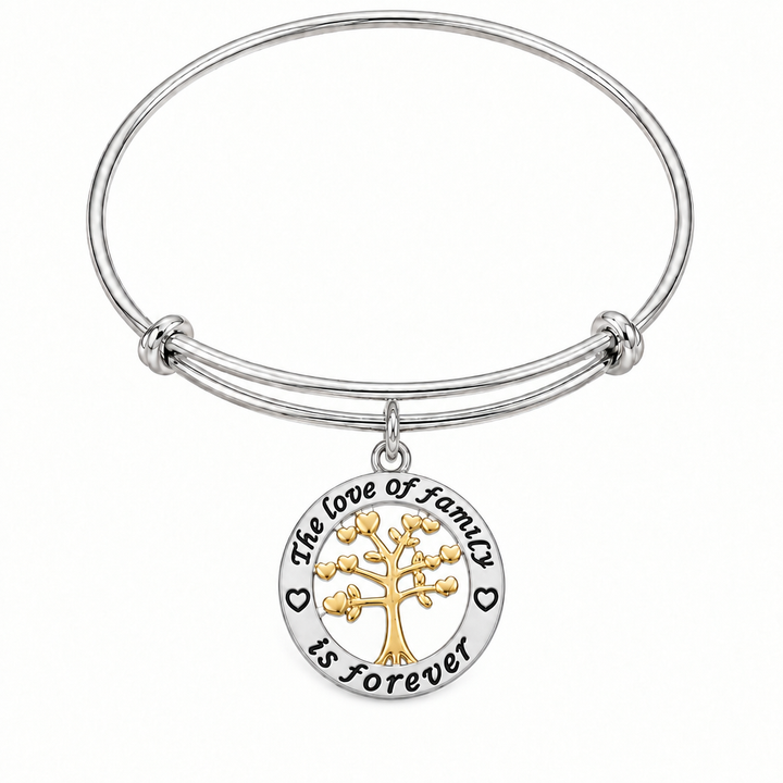 Silver bangle bracelet with a round pendant engraved "The love of family is forever" featuring a gold tree of life with heart leaves, shown on a warm-white studio background