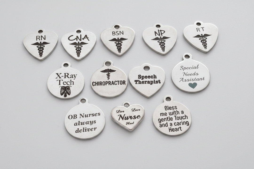 Collection of silver stainless steel engraved charms for healthcare professionals including RN, CNA, BSN, NP, RT, X-Ray Tech, Chiropractor, Speech Therapist, Special Needs Assistant, and nurse-themed sentiment charms, arranged on a light background with studio lighting
