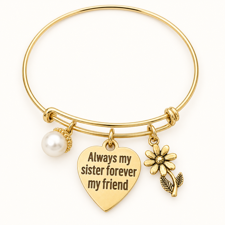 Gold bangle bracelet with a heart charm engraved Always my sister forever my friend, a pearl charm, and a gold daisy charm, shown on a warm-white studio background