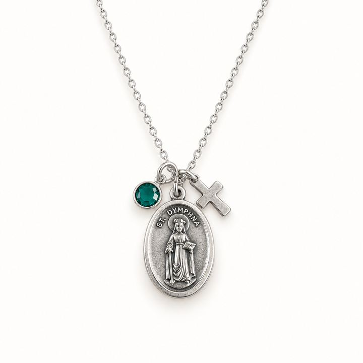 Saint Dymphna necklace with silver medal, cross charm, and crystal birthstone on a warm white studio background