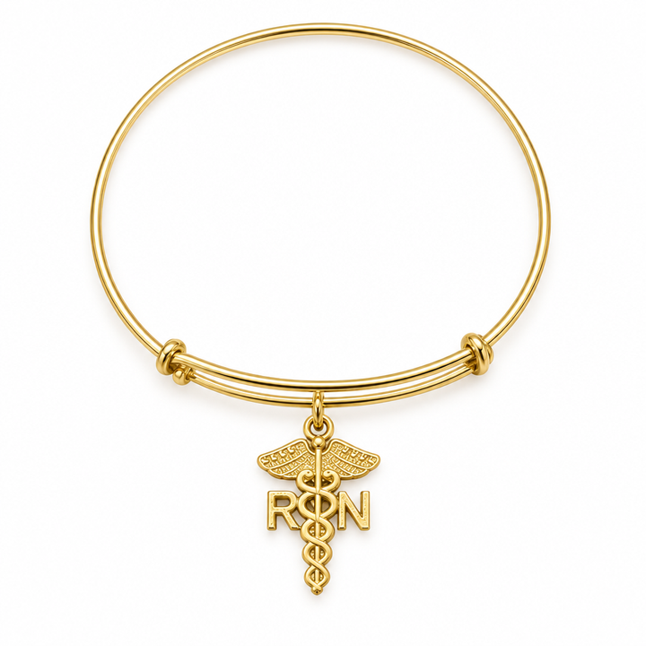Gold bangle bracelet with a caduceus medical symbol charm and RN letters, shown on a warm-white studio background